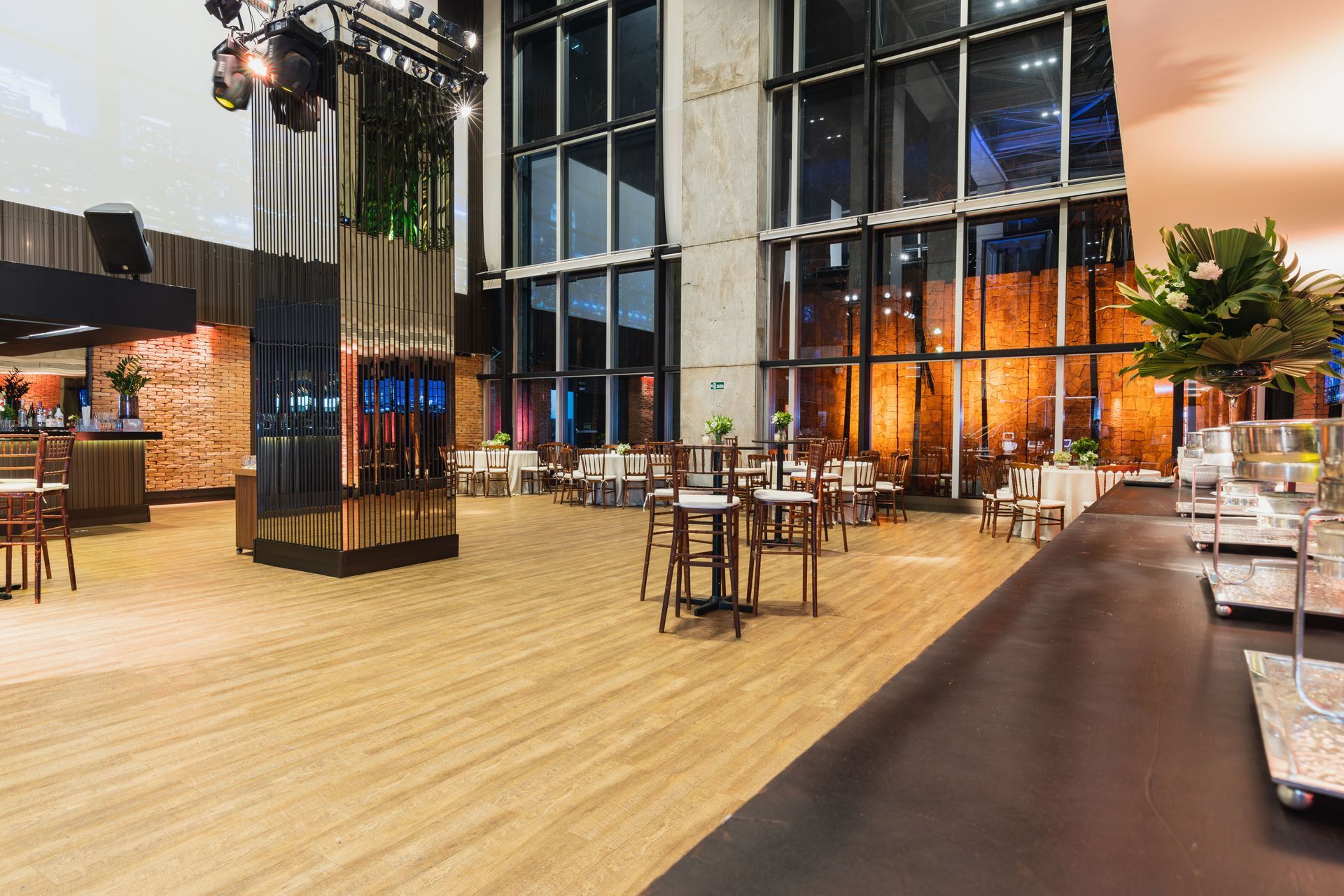 Interior de restaurante moderno con suelos de madera, grandes ventanales, asientos en la barra e iluminación cálida.