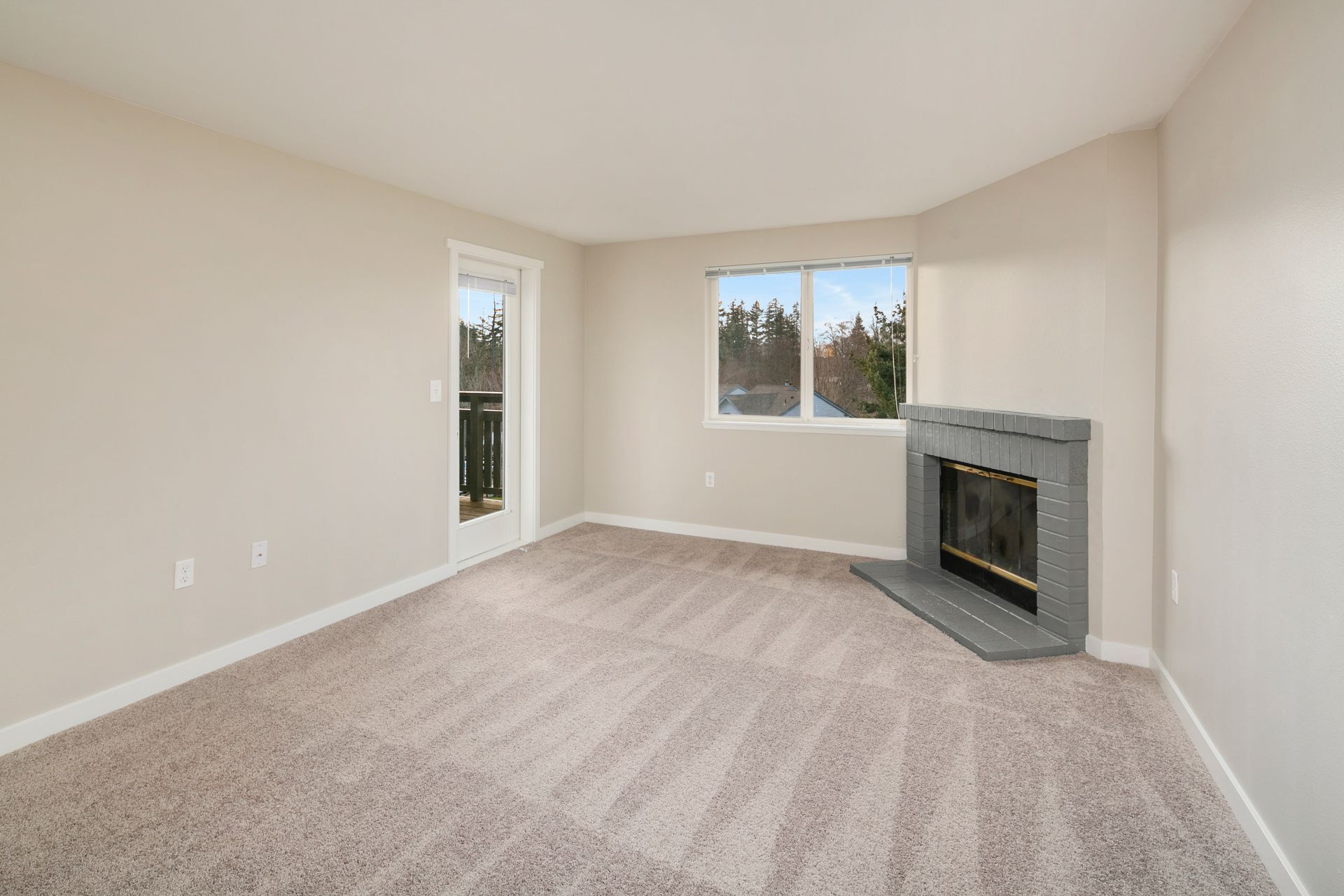 An empty living room with a fireplace and a balcony.