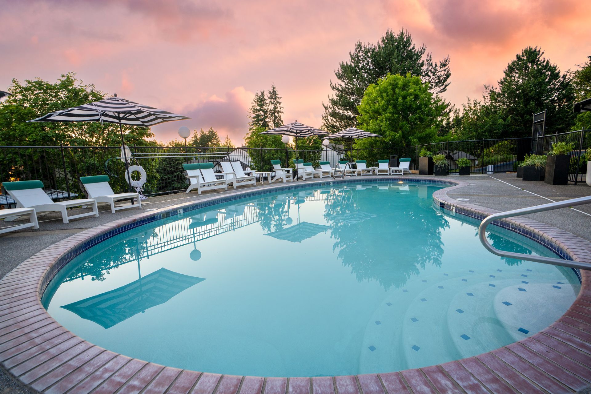 A large swimming pool surrounded by chairs and umbrellas at sunset.