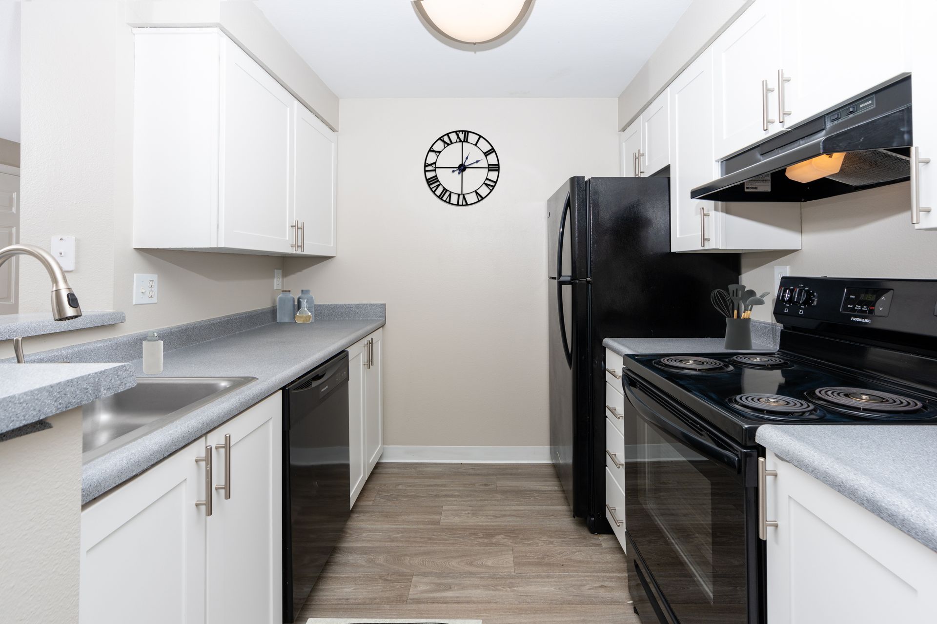 A kitchen with white cabinets, black appliances, and a clock on the wall.