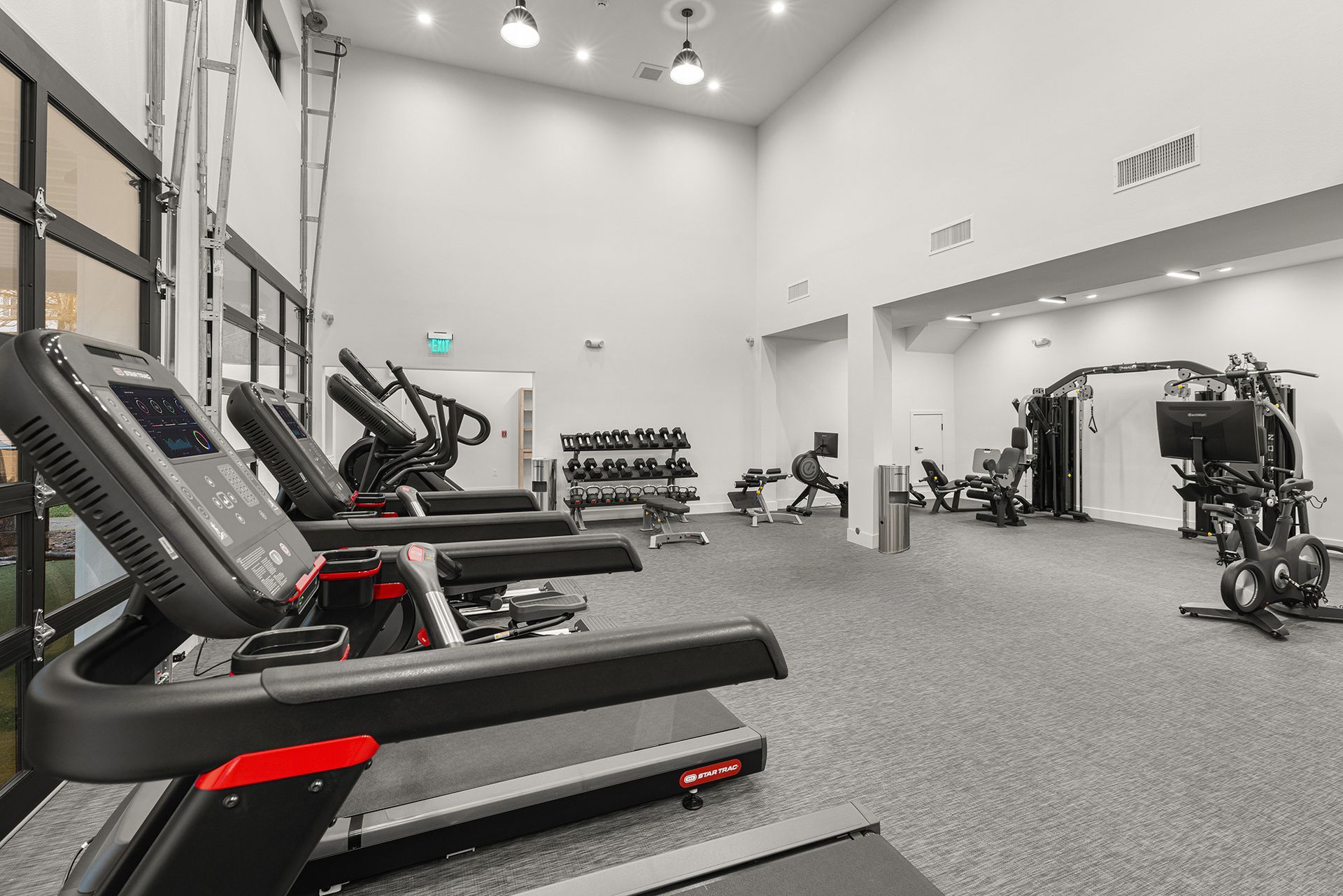Gym with treadmills, weights, and exercise machines; white walls, gray floor.