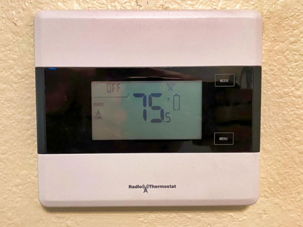 White digital thermostat displaying 75°F on a wall.