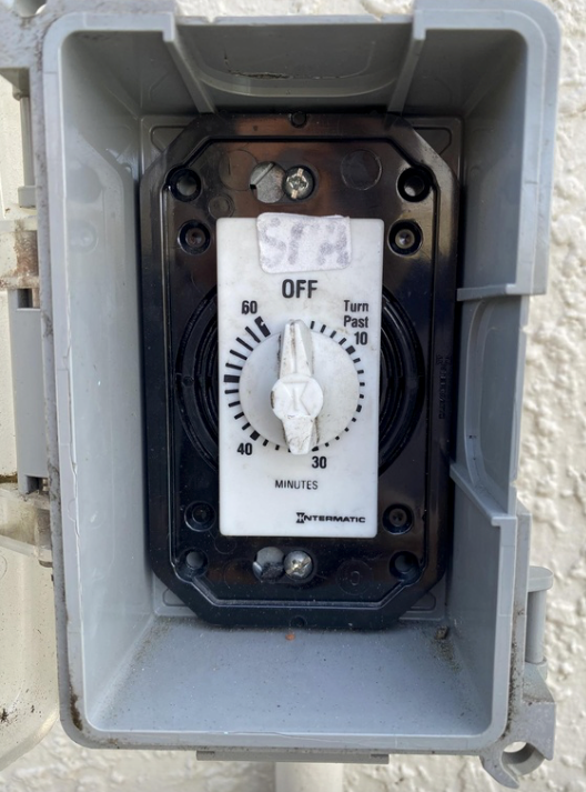 Outdoor electrical timer switch in gray enclosure, set to OFF with a dial and labeled fan, pump, and pool.