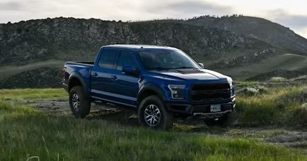 Blue pickup truck driving on a grassy field with hills in the background