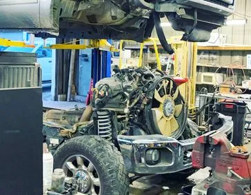 Truck chassis in a shop with engine exposed, supported on a lift.