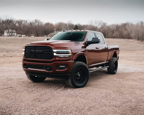 Maroon pickup truck with black rims parked on a gravel lot under an overcast sky