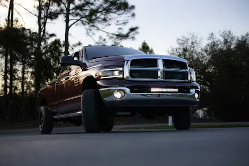 Maroon pickup truck driving on a road at dusk with trees in the background