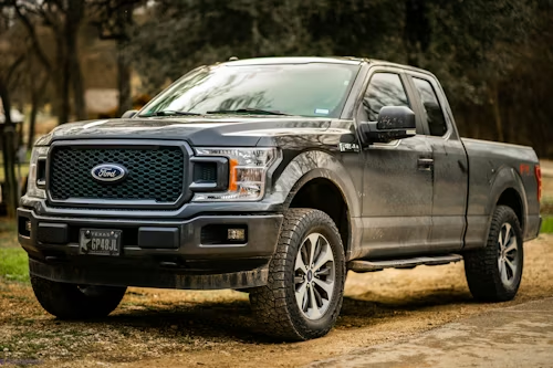 Black Ford F-150 pickup truck parked on a dirt path in a wooded area
