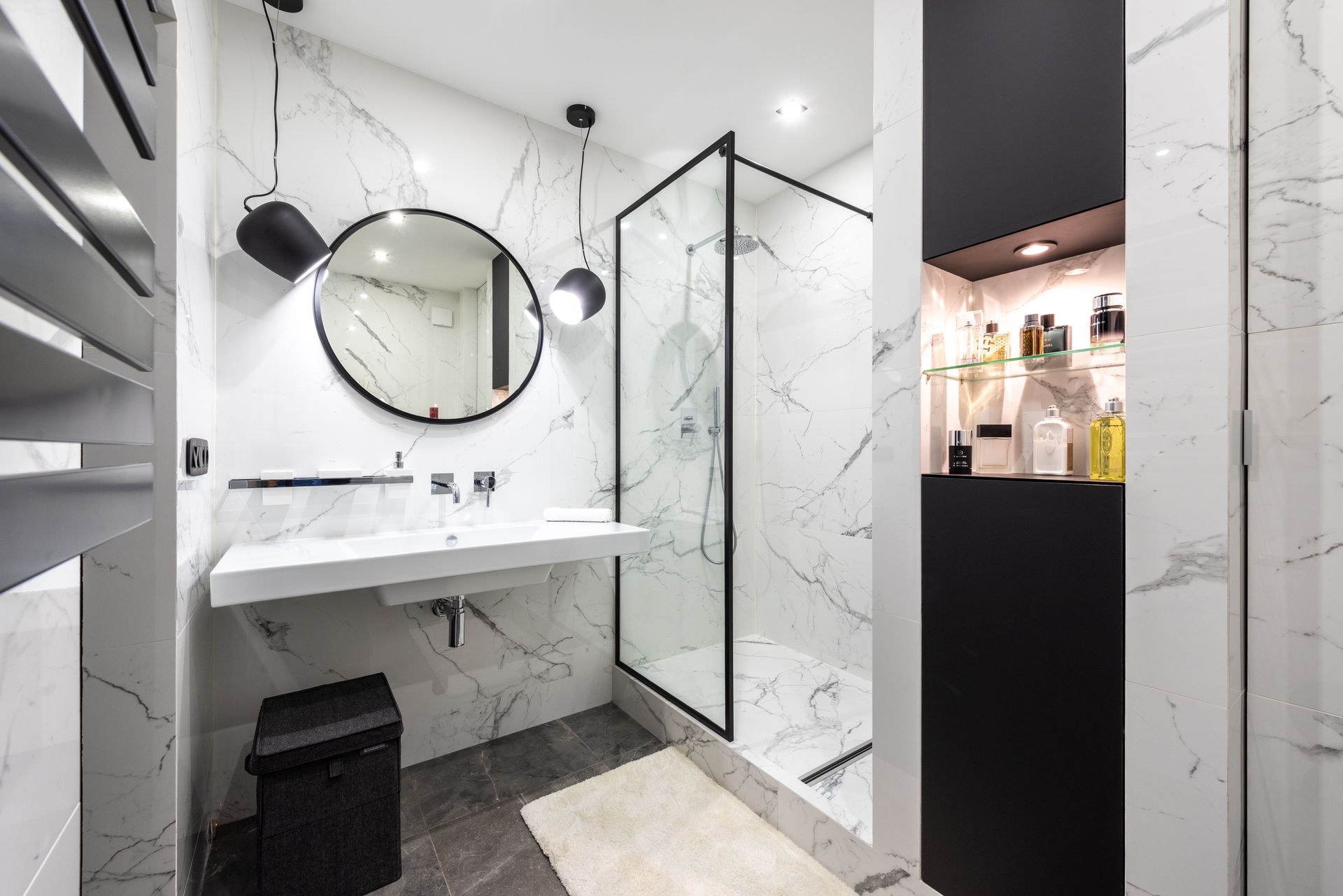 Modern black-and-white bathroom with marble shower, round mirror, and floating sink