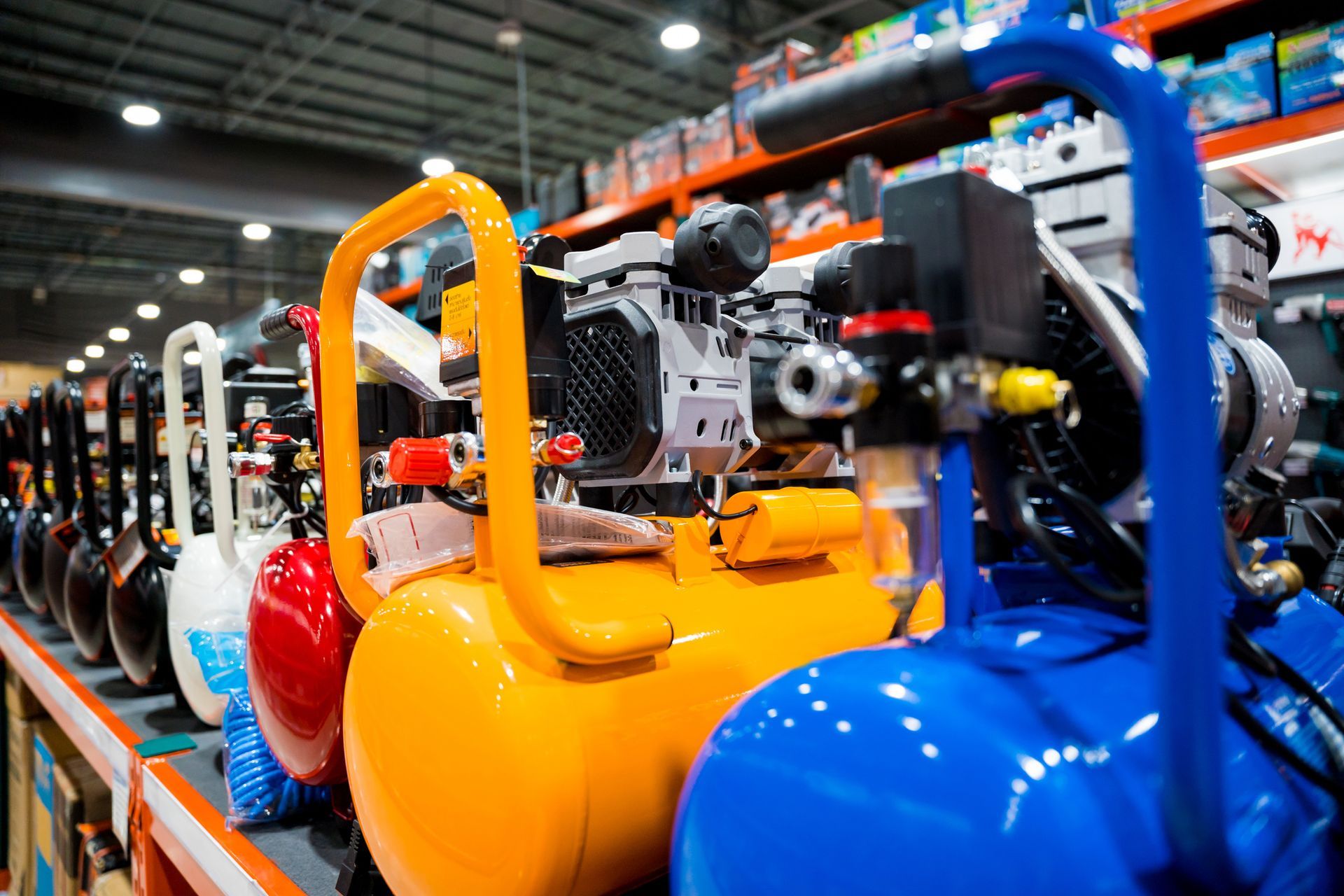 Row of colorful air compressors displayed on shelves in a hardware store.