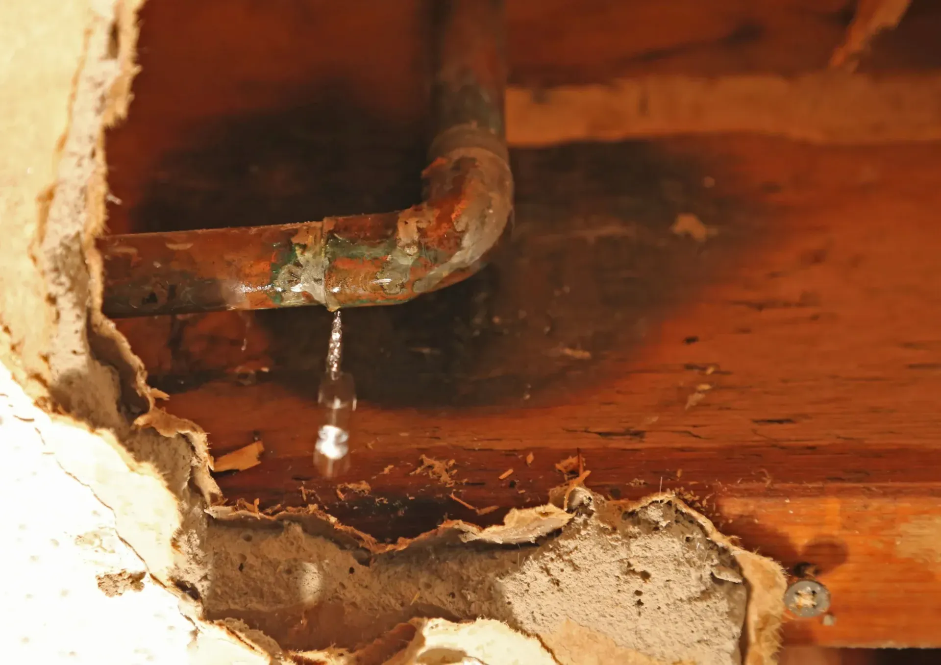 Leaking rusty pipe dripping water onto a damaged wooden floor with peeling plaster