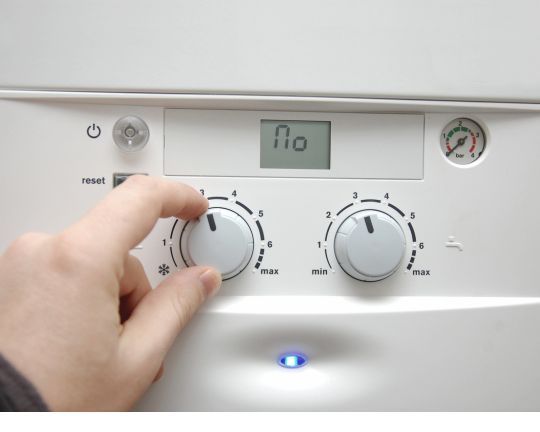 Hand adjusting a white boiler control knob with digital display and two dials