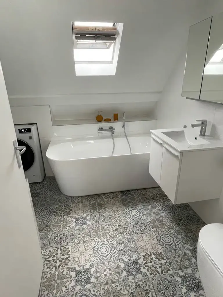 Compact attic bathroom with bathtub under a skylight, sink, patterned tile floor, and washing machine in the corner