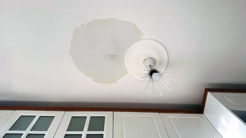 Ceiling with a large water stain and a cracked light fixture above kitchen cabinets