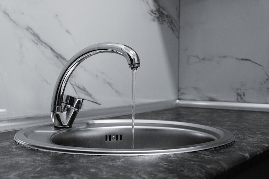 Chrome faucet running into a stainless steel kitchen sink with marble backsplash
