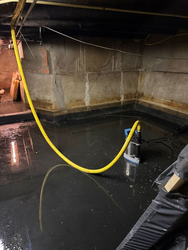 Flooded basement with standing black water, cinder block walls, and a yellow hose suspended overhead