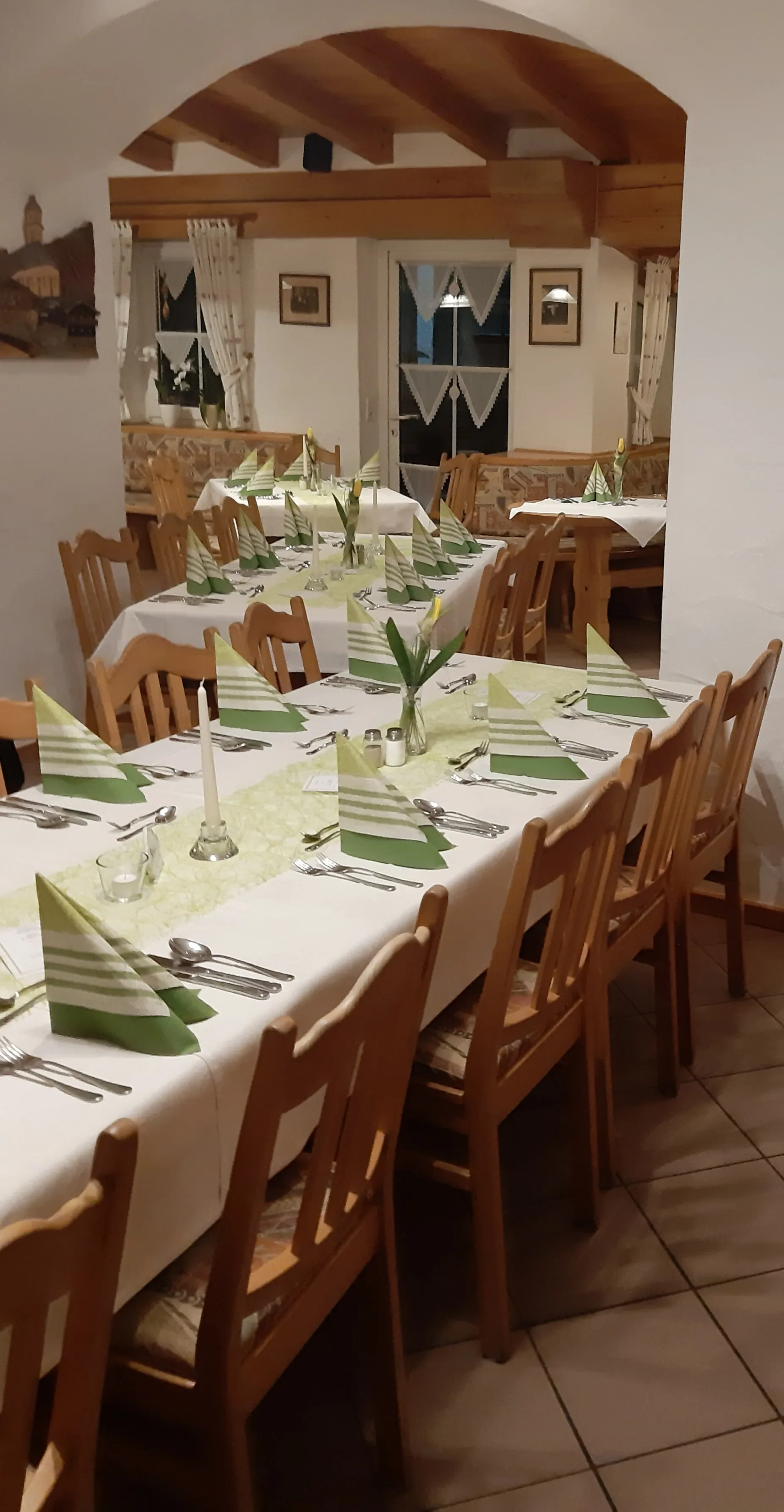 Ein langer Tisch mit einer weißen Tischdecke und Holzstühlen in einem Restaurant.