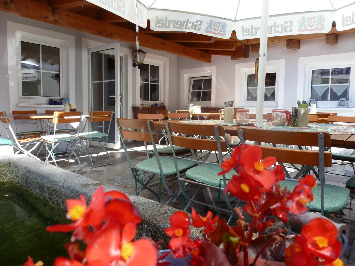Eine Terrasse mit Tischen und Stühlen unter einem Sonnenschirm und Blumen im Vordergrund