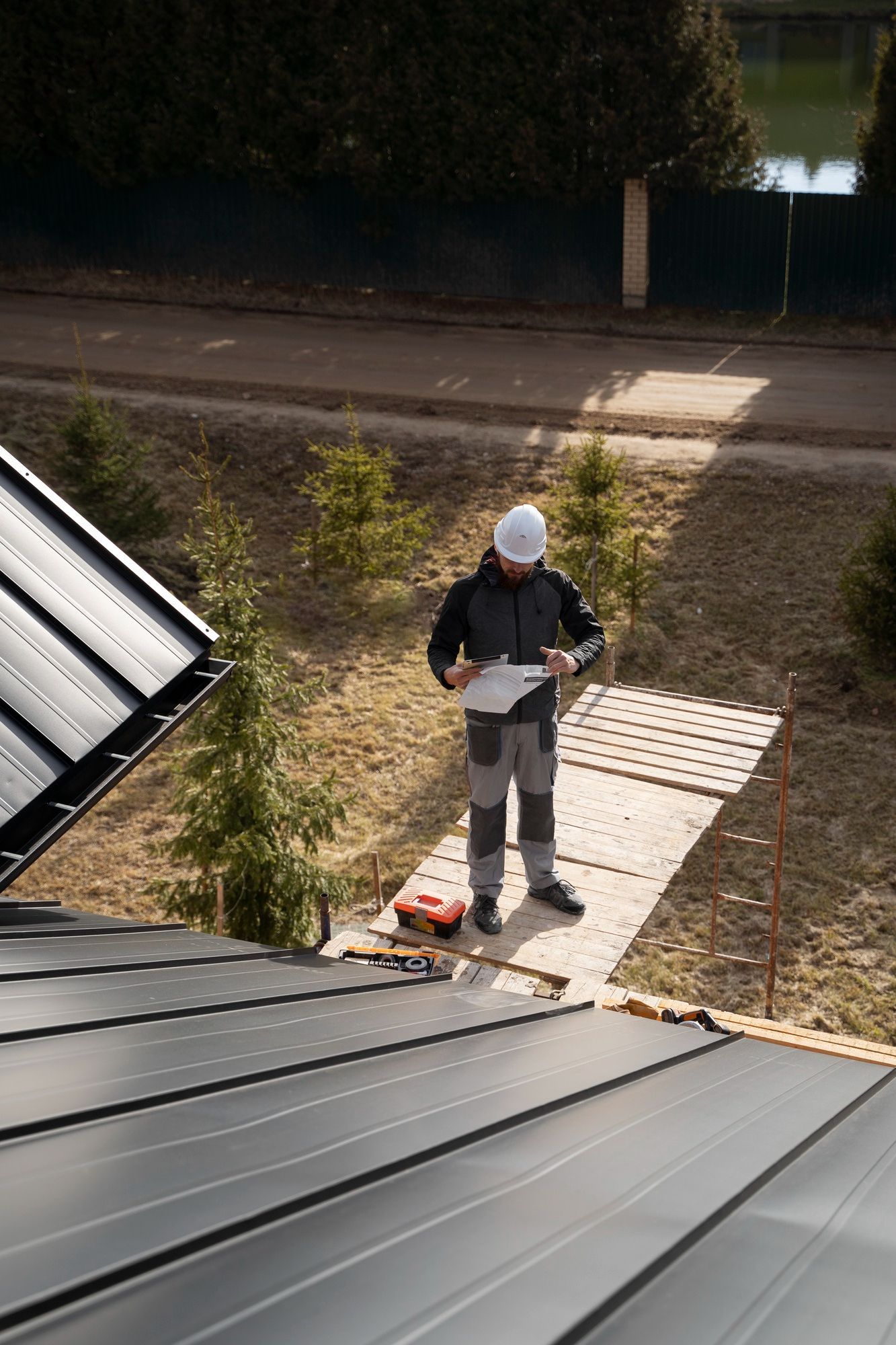 Worker in hard hat inspecting a roof near a roof edge, holding a clipboard on a sunny day