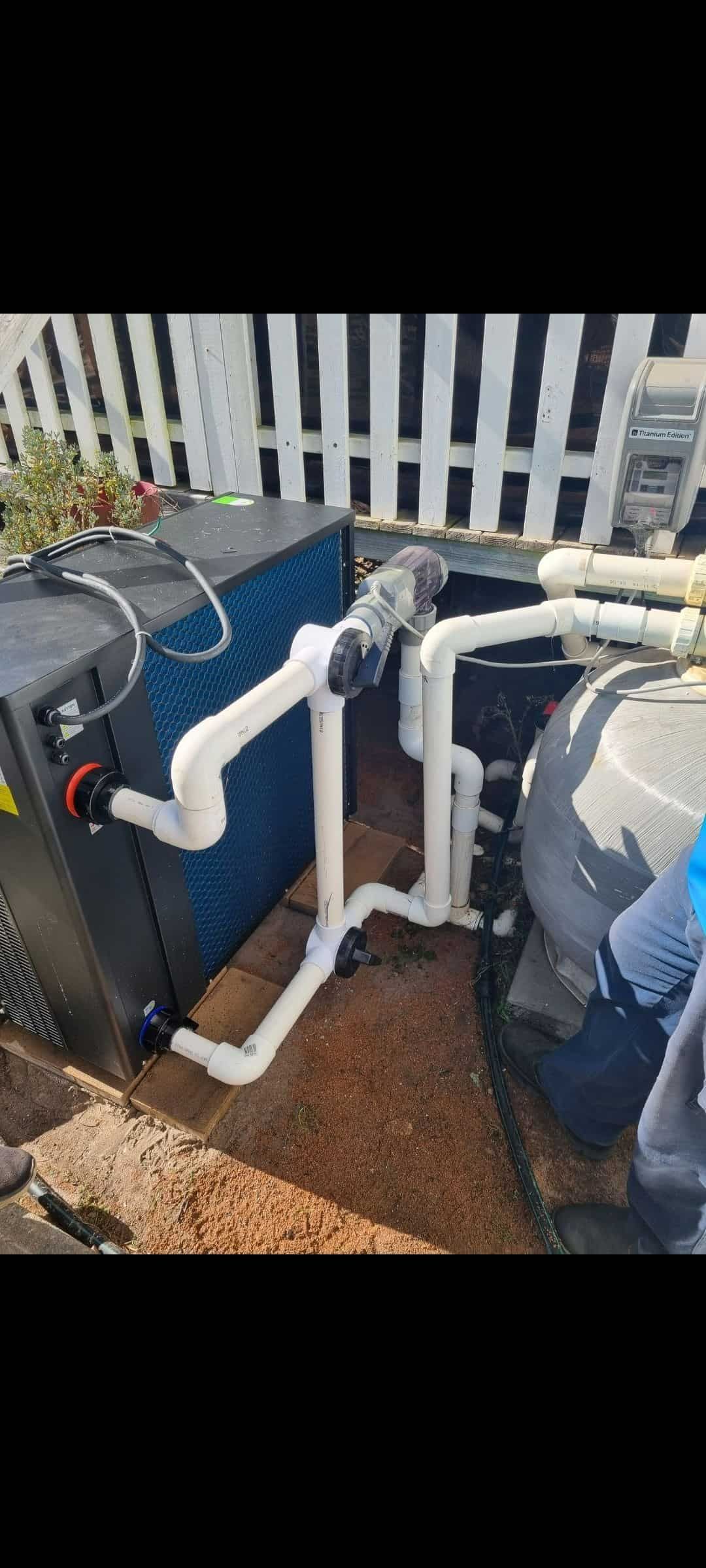 A Pool Heater Is Sitting On The Ground Next To A White Fence — Manning Pools, Rubber & Foam In Taree, NSW