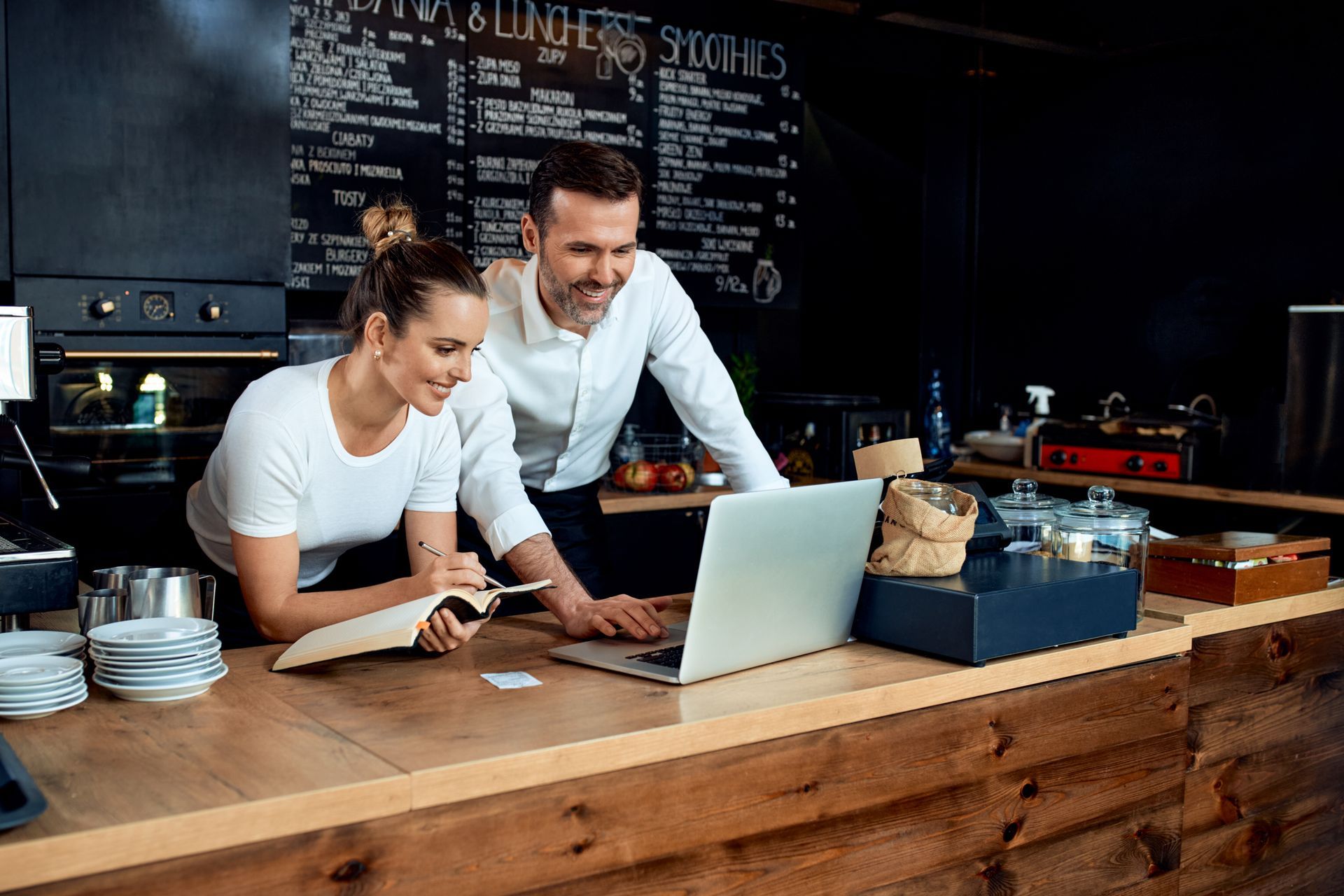 a man and a woman are looking at a laptop in a restaurant