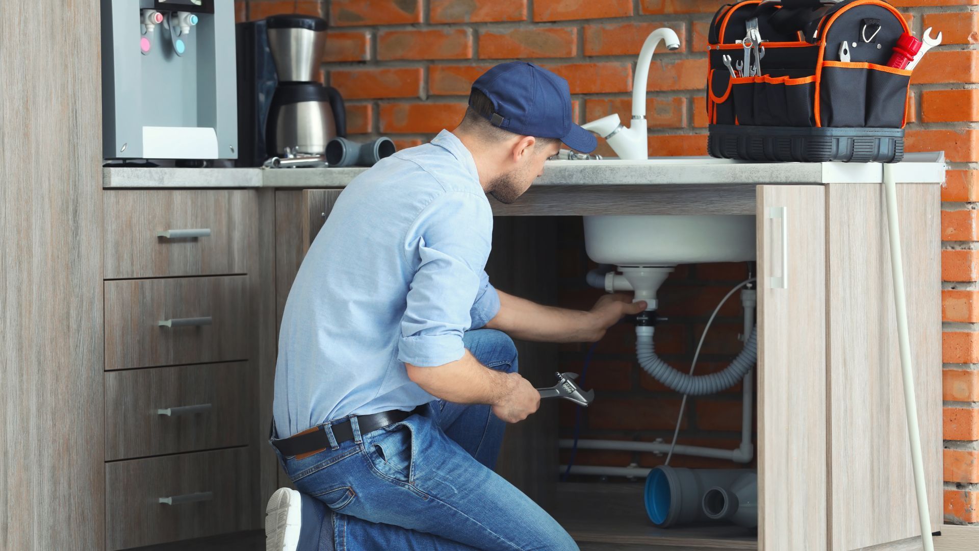 A plumber is fixing a sink in a kitchen.
