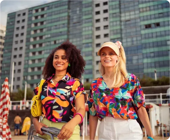 Two women are walking on a beach in front of a building.
