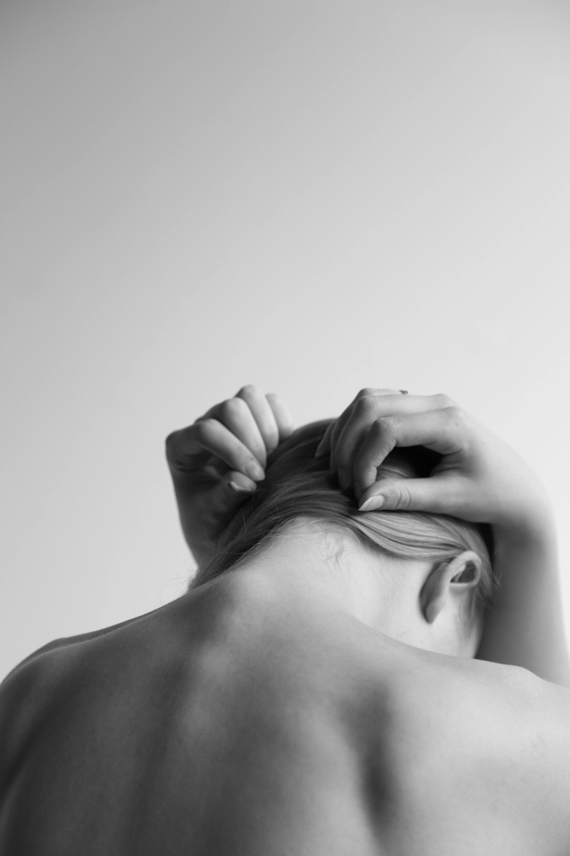 Una fotografía en blanco y negro de la espalda de una mujer con las manos en el cabello.
