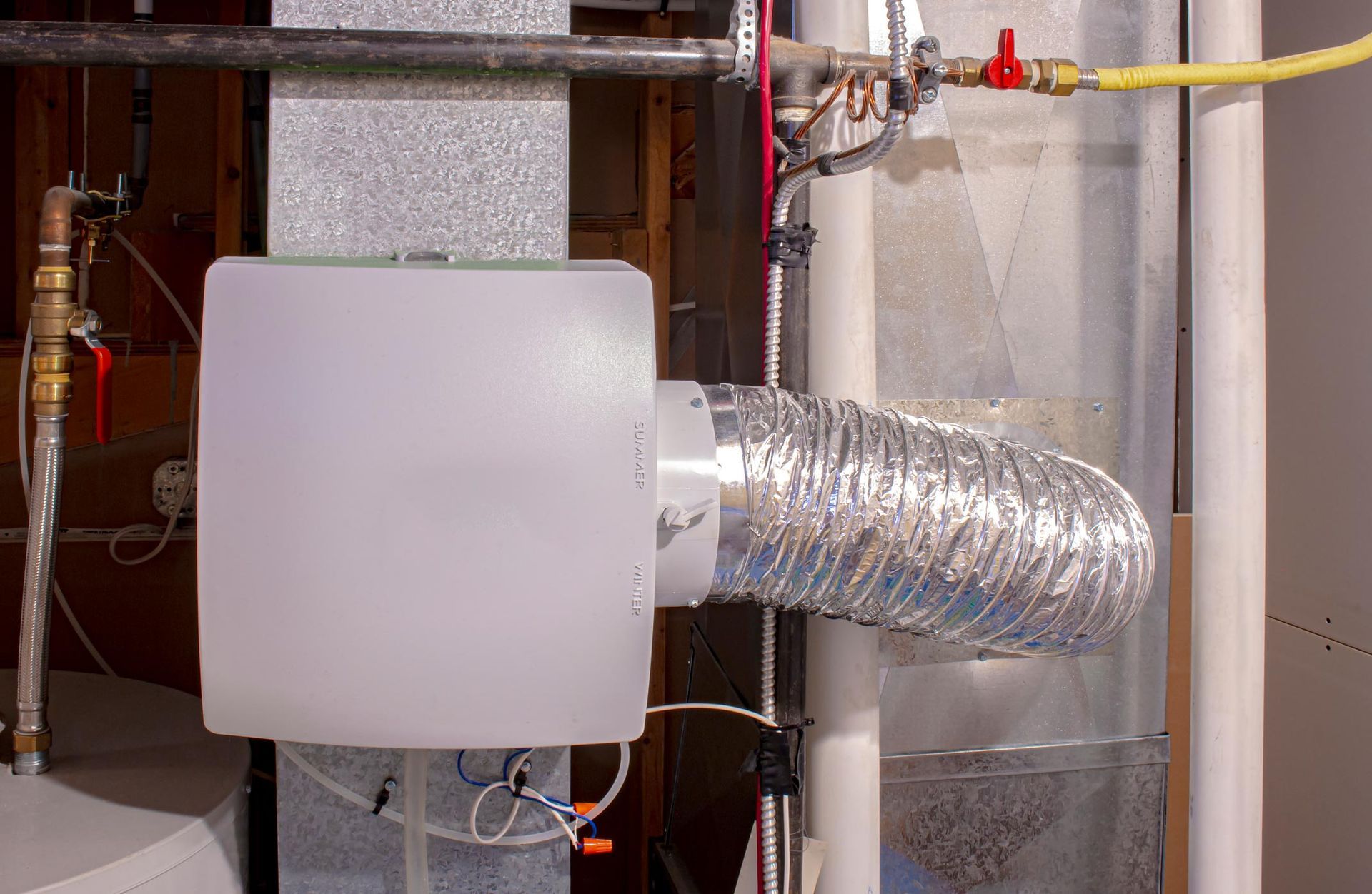 A white box is sitting on top of a metal pipe in a basement.