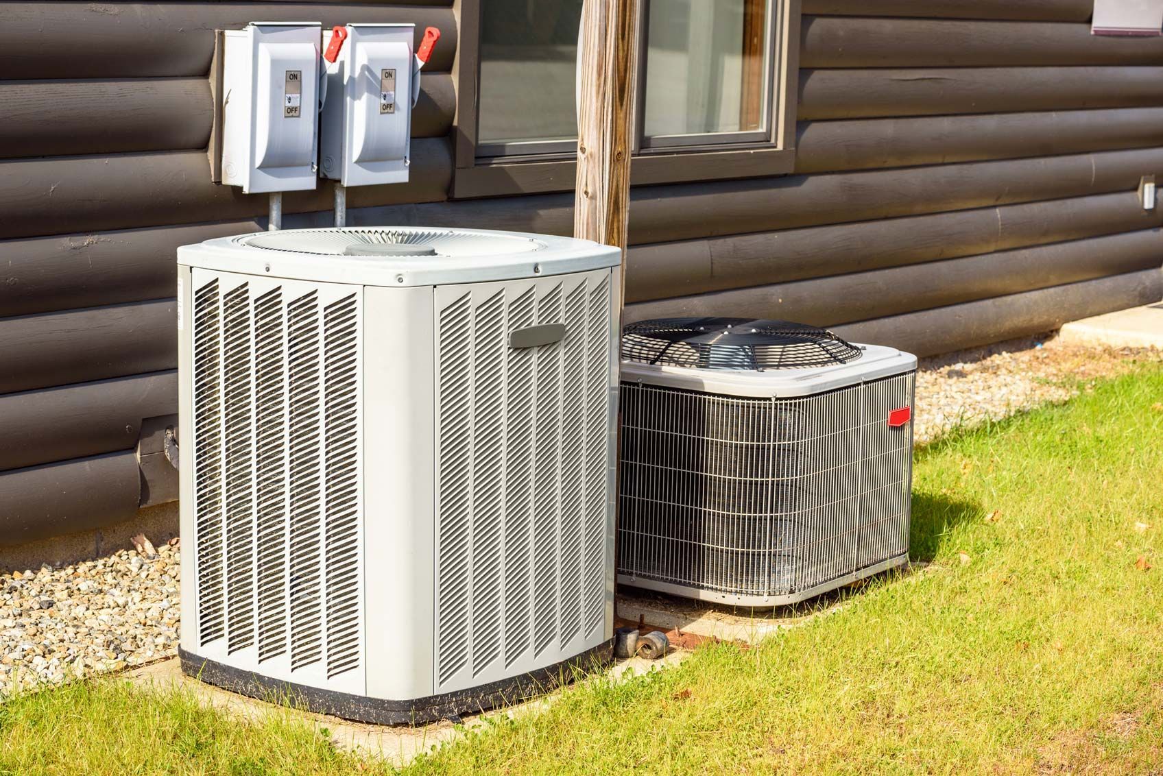 Two air conditioners are sitting on the side of a log cabin.