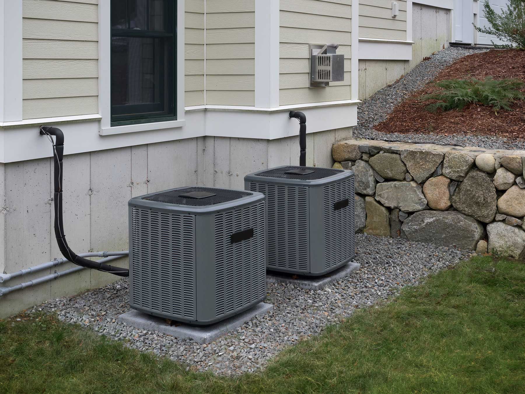 Two air conditioners are sitting on the side of a house.