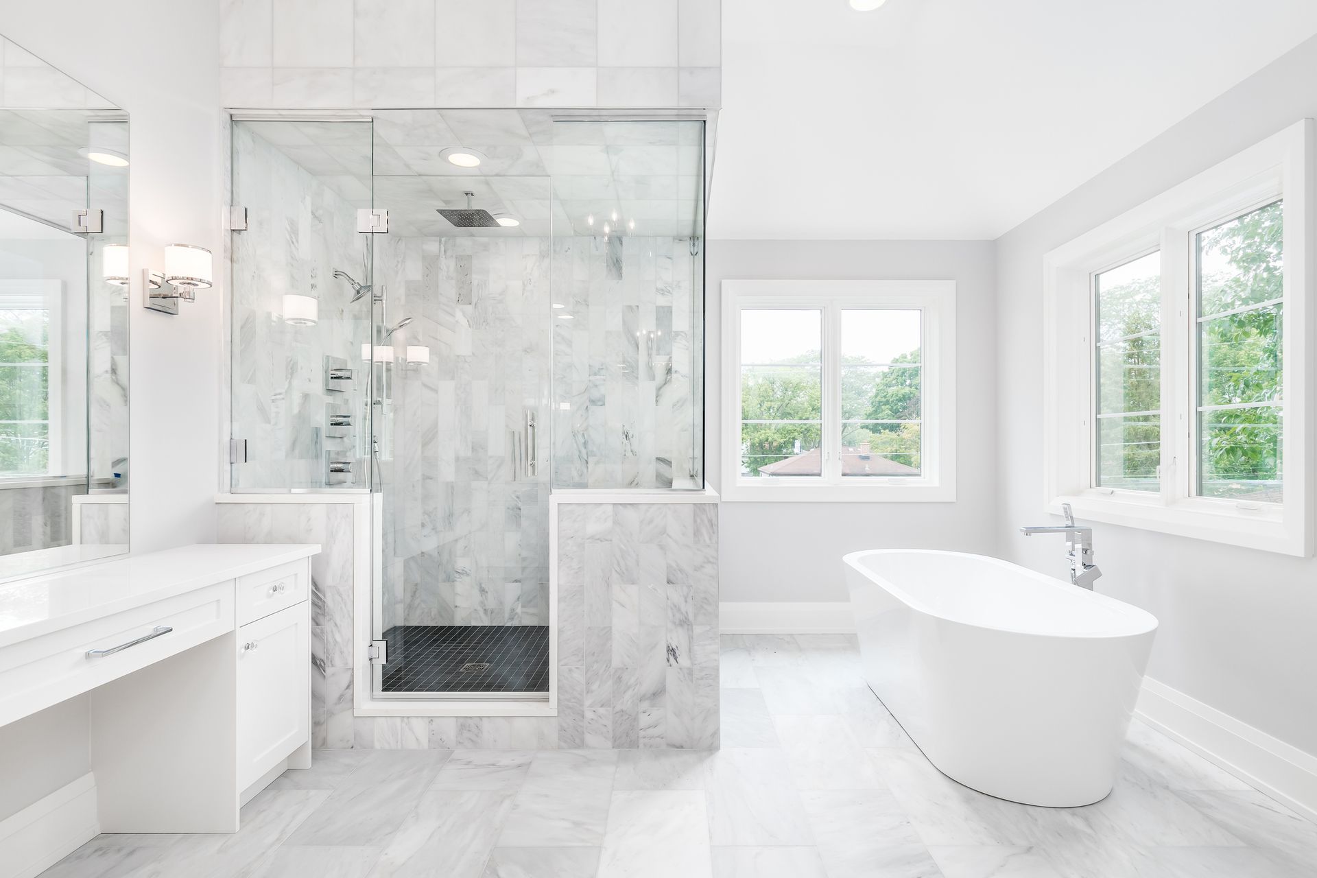 Bright white bathroom with marble tile, glass shower, freestanding tub, and windows.