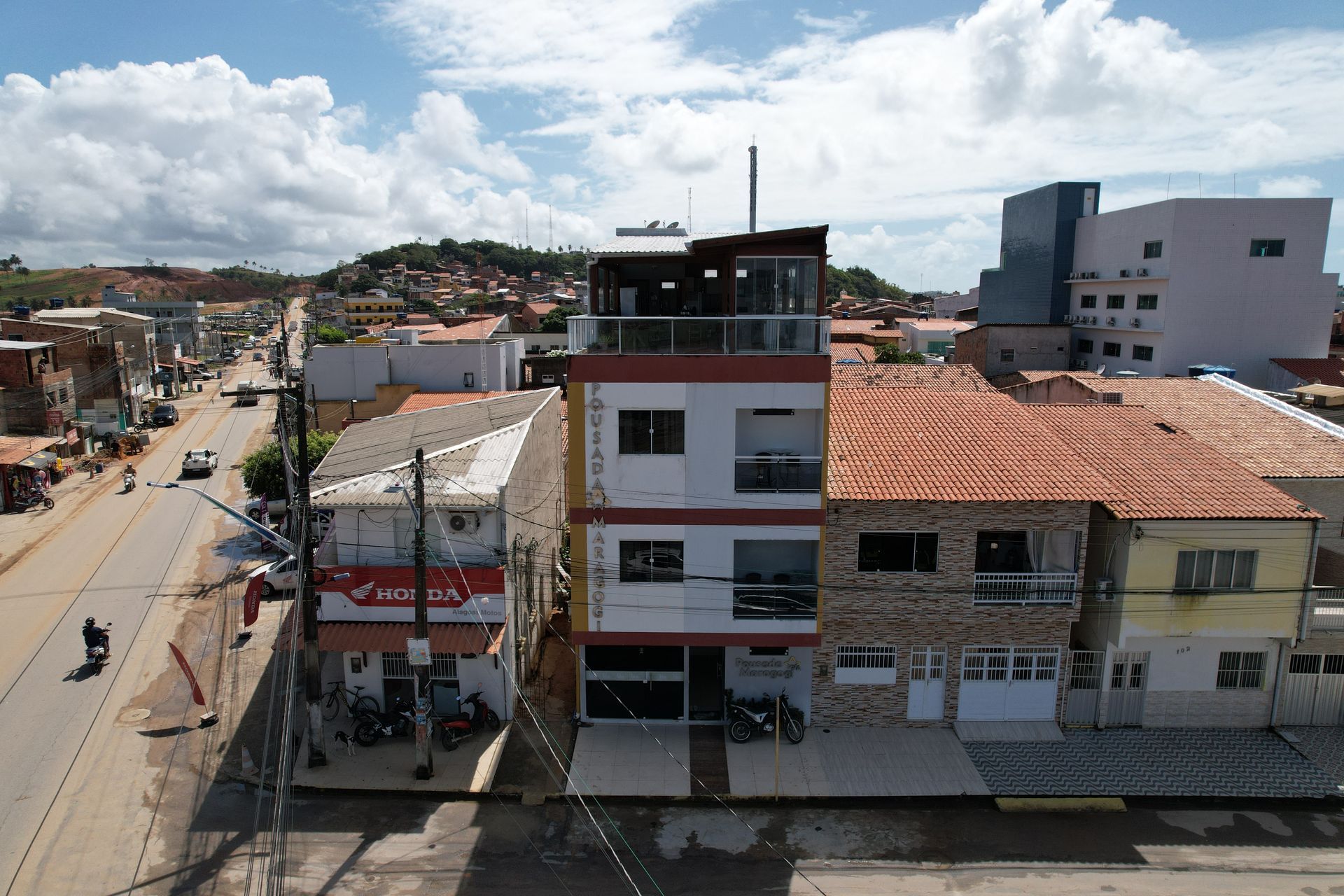 Vista aérea de uma rua com prédios baixos, telhados de terracota e céu nublado.