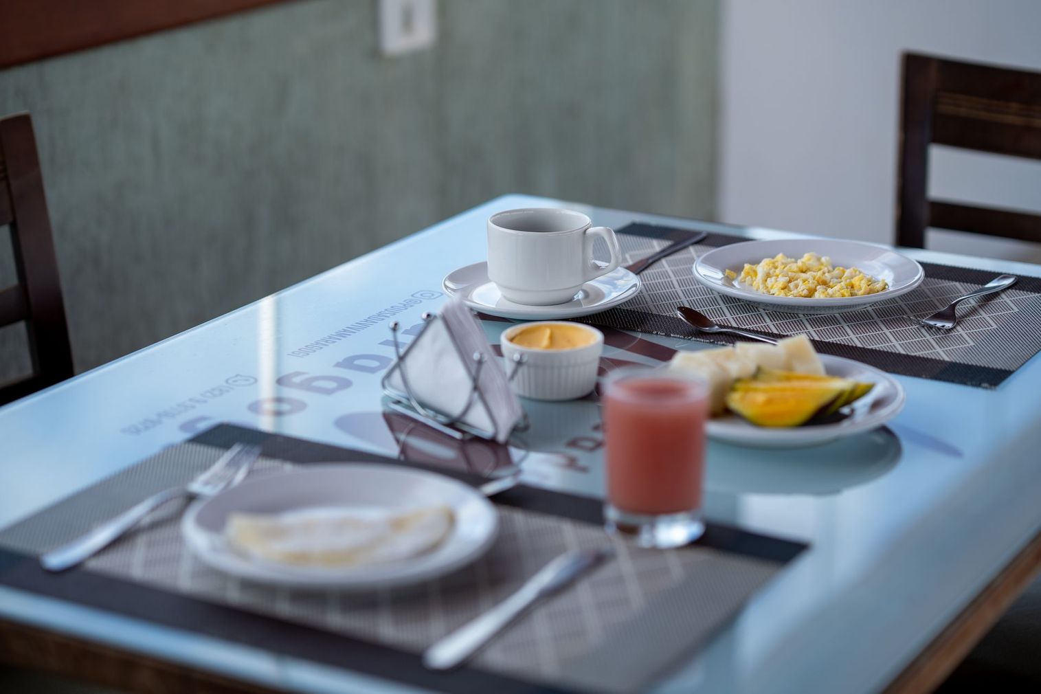 Café da manhã servido em uma mesa de jantar com café, frutas, suco e doces.