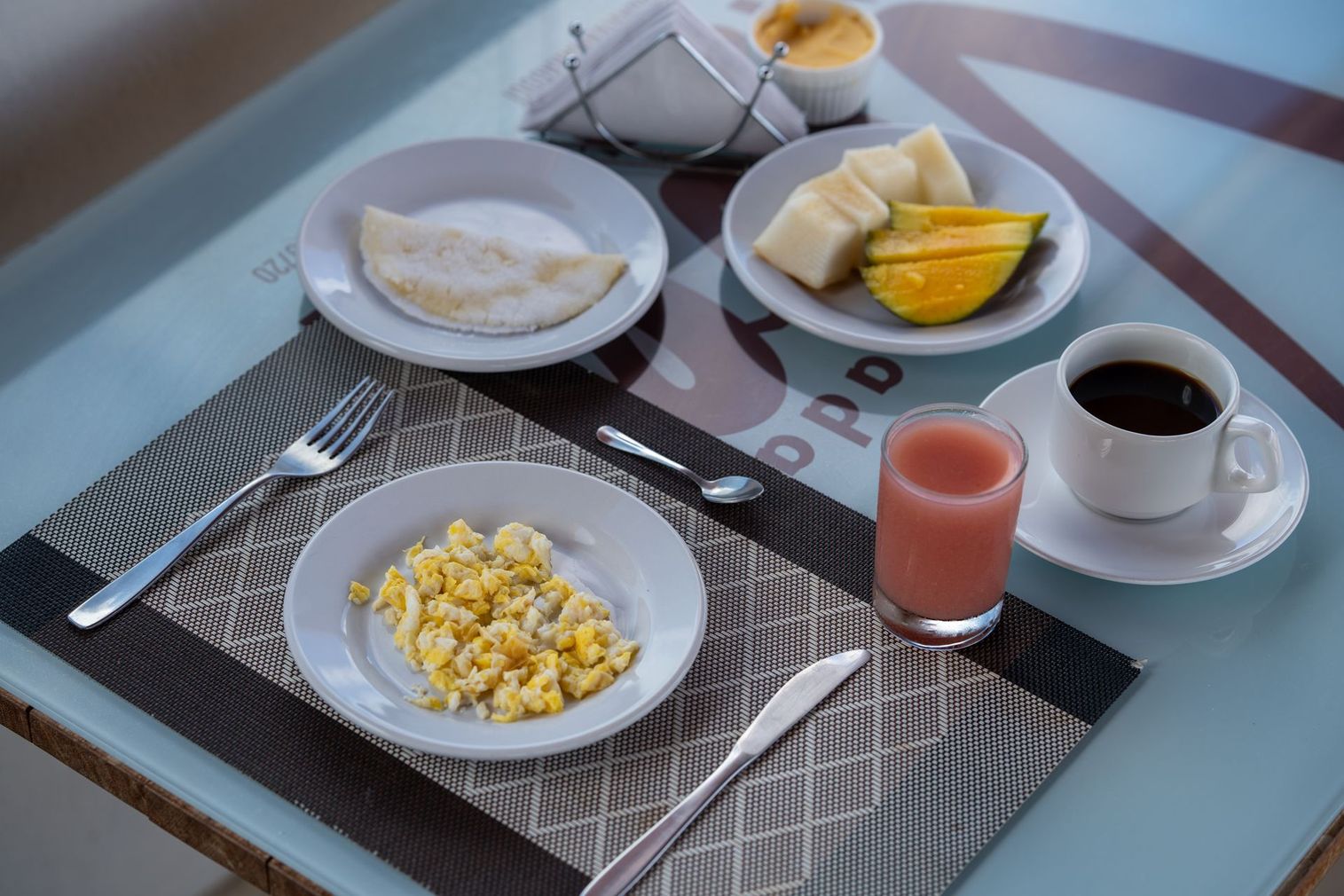 Bandeja de café da manhã com café, suco, ovos mexidos, frutas e torradas em uma mesa de colo
