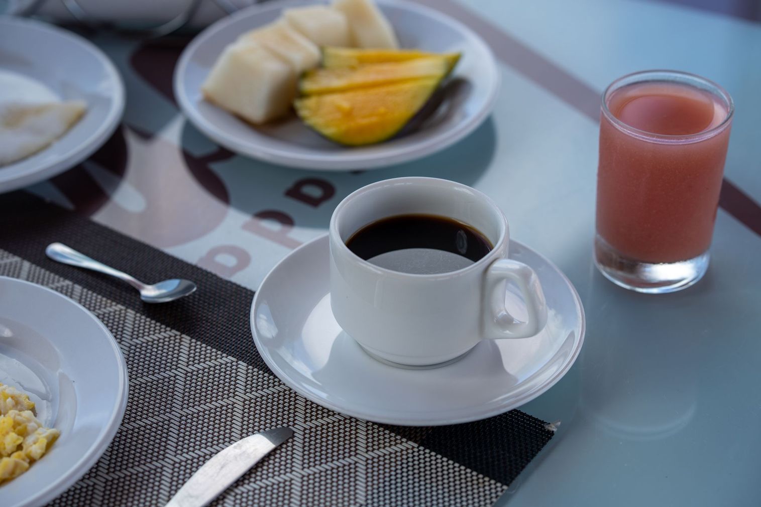 Mesa de café da manhã com café, frutas, cereais e um copo de suco rosa.