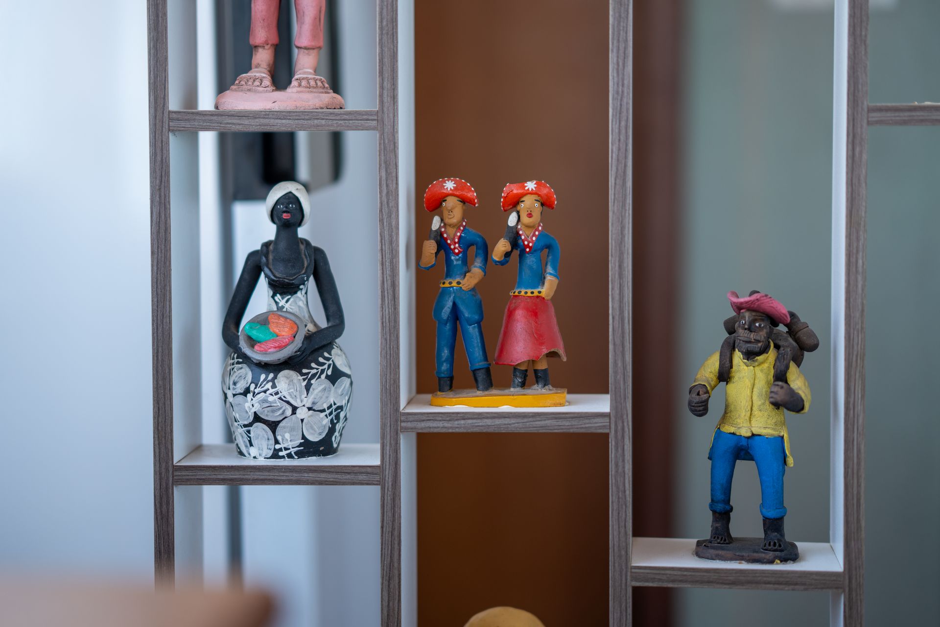Miniaturas expostas em prateleiras, incluindo duas figuras coloridas e uma figura sentada em preto e branco.
