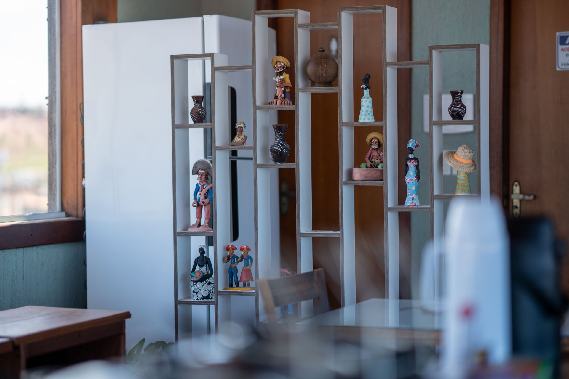 Quarto moderno com um armário de madeira exibindo estatuetas ao lado de uma geladeira branca e uma janela.