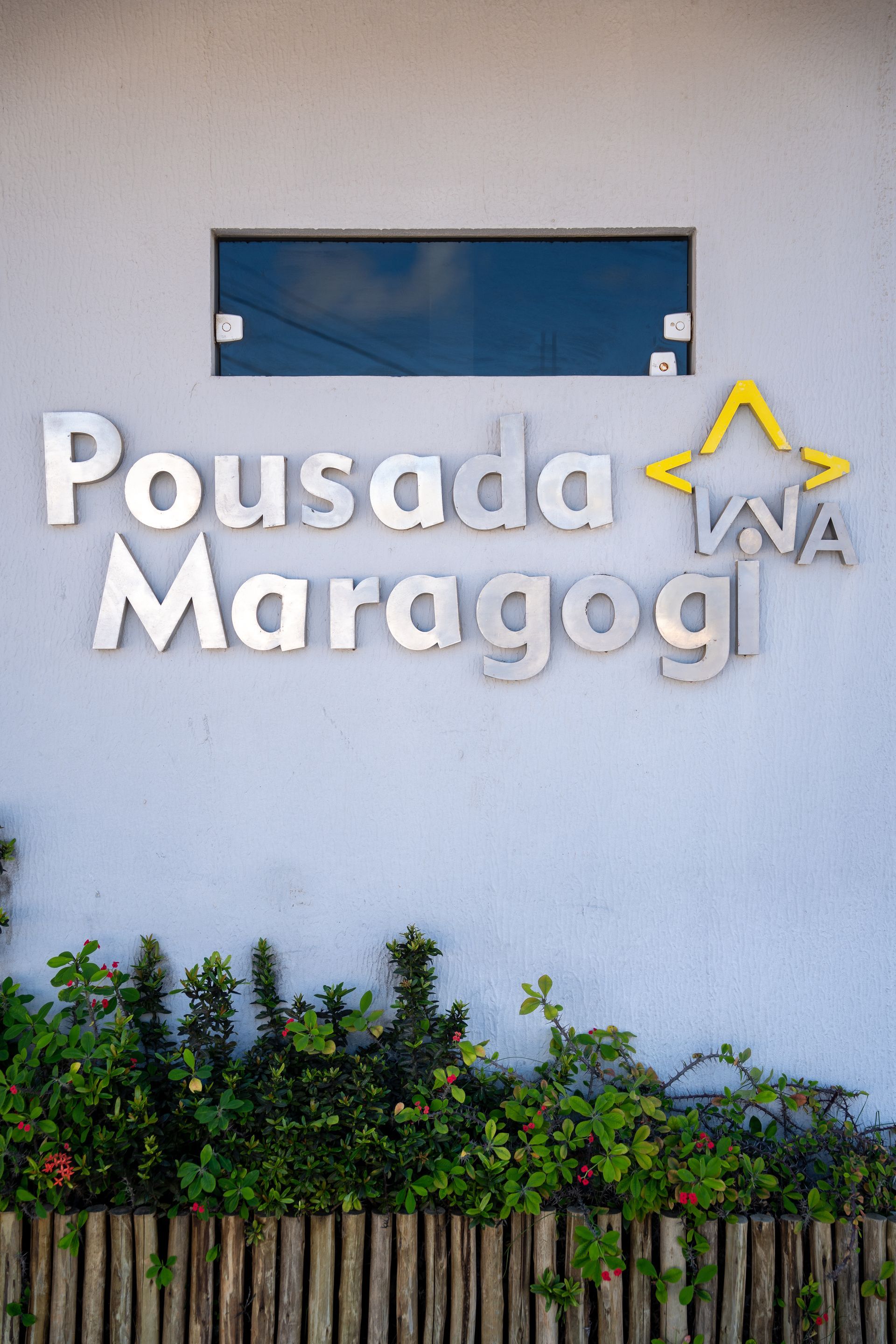 Placa da Pousada Maragogi em uma parede branca acima da vegetação.