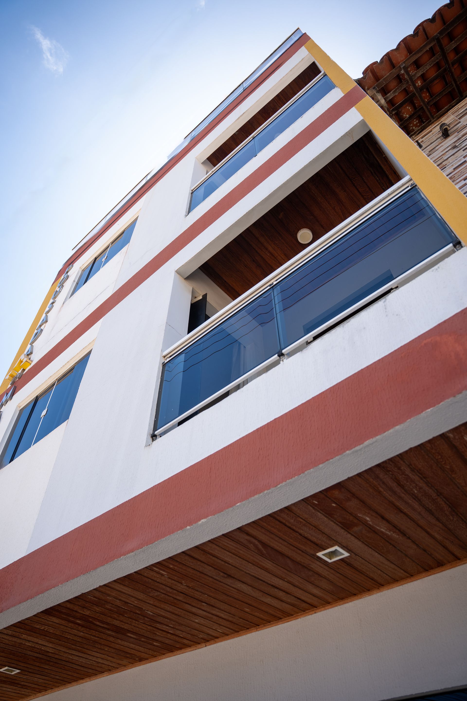 Vista em ângulo baixo de um prédio de apartamentos moderno com paredes brancas, varandas azuis e detalhes em vermelho.
