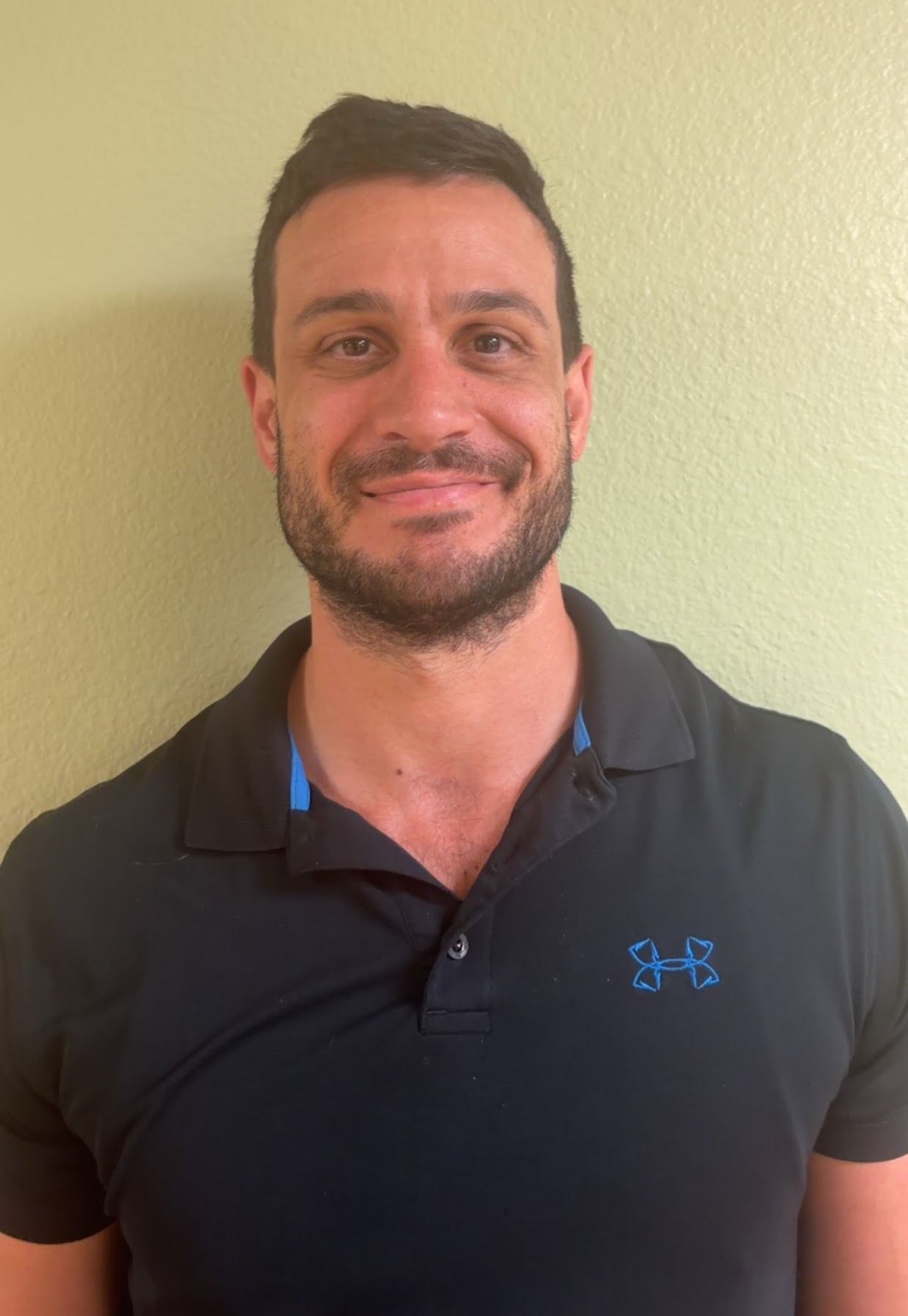 Man with a beard wearing a dark blue polo shirt with a logo.