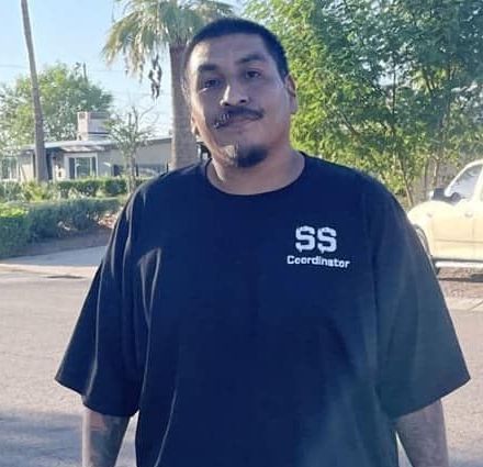 Man with a mustache wearing a dark blue t-shirt that says 