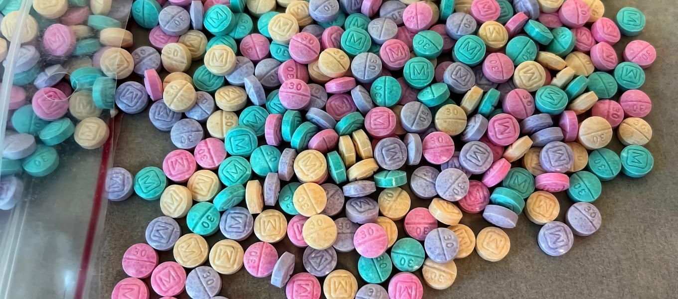 Pile of colorful pills, mostly turquoise, pink, purple, and yellow, spilled from a clear plastic bag.