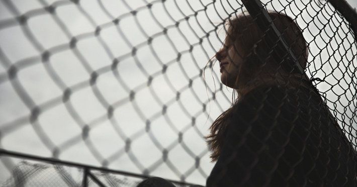 Woman behind chain-link fence, looking up, with overcast sky.