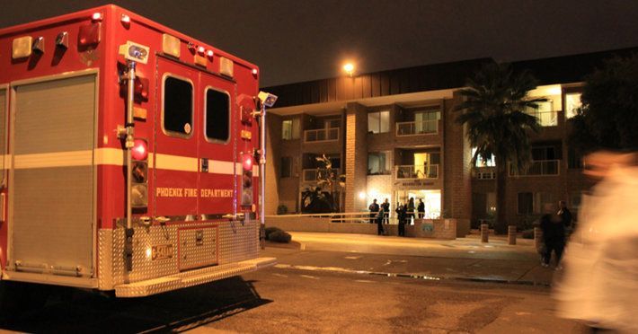 Fire truck at night in front of an apartment building, with people gathered and lights on.