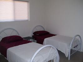 Two twin beds with white frames, burgundy bedding, in a room with a window.