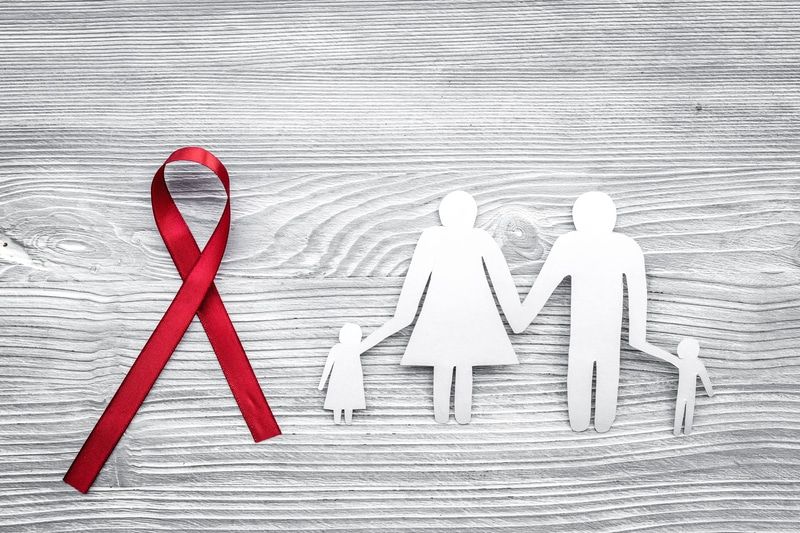 Red ribbon and paper family on gray wood background, symbolizing AIDS awareness.