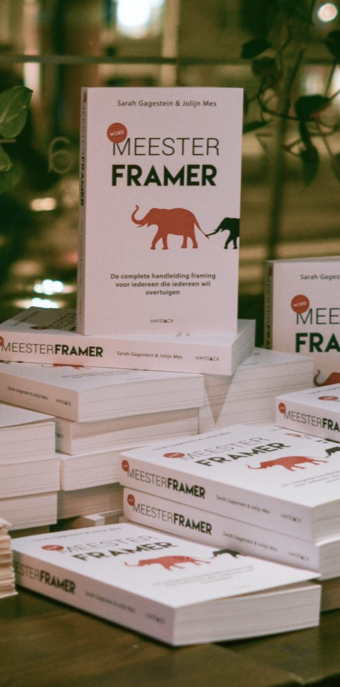 Op een tafel liggen stapels witte boeken met een rood dier op de omslag, getiteld 