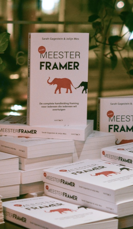 Een stapel boeken met een oranje olifant op de kaft en als titel 'Word Meesterframer', tentoongesteld op een stand.
