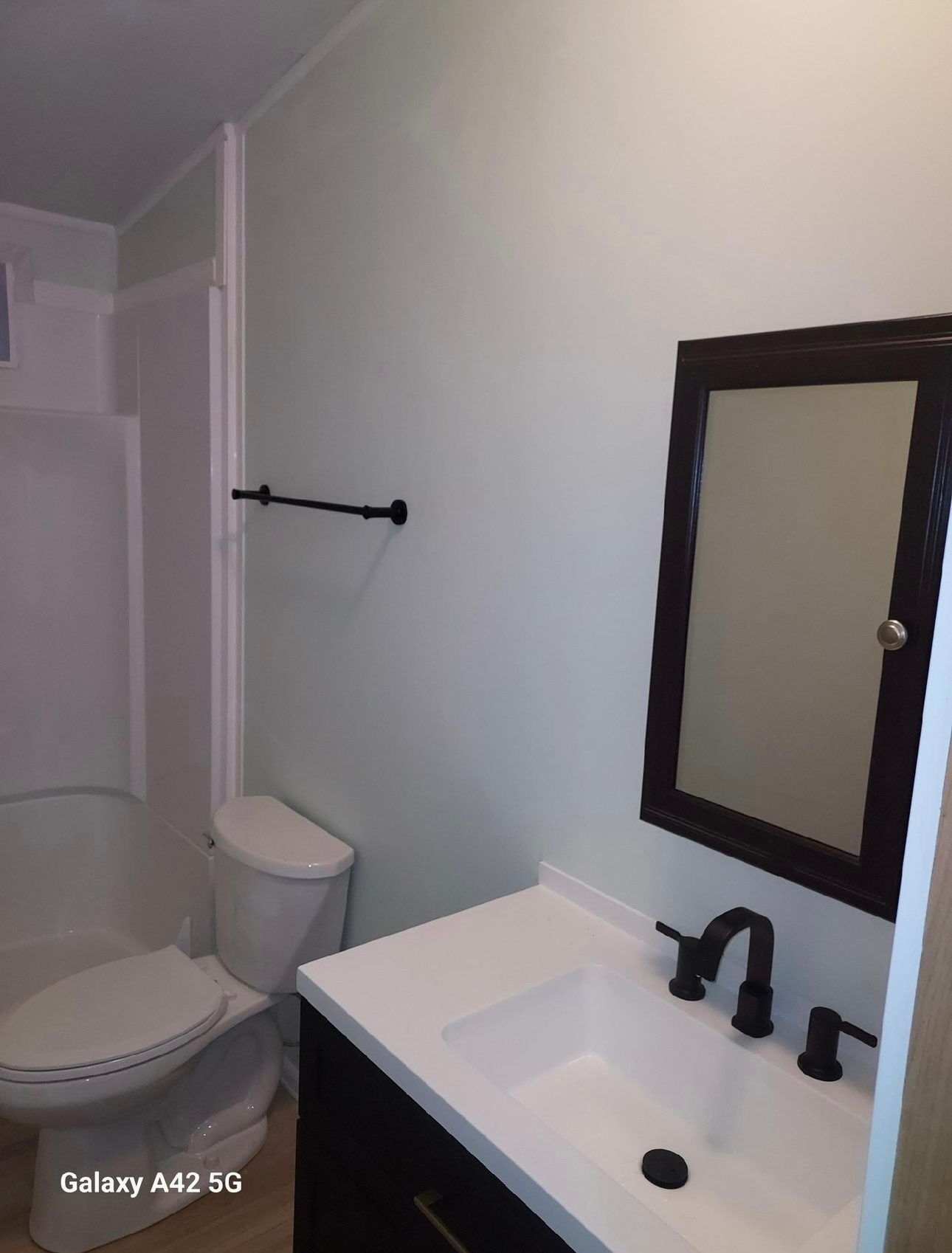 A modern bathroom featuring a white vanity with black fixtures, a mirror cabinet, and a toilet next to a shower unit.